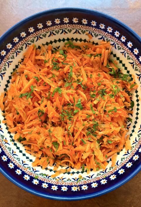 Classic grated carrot salad with fresh parsley in a blue Polish pottery bowl