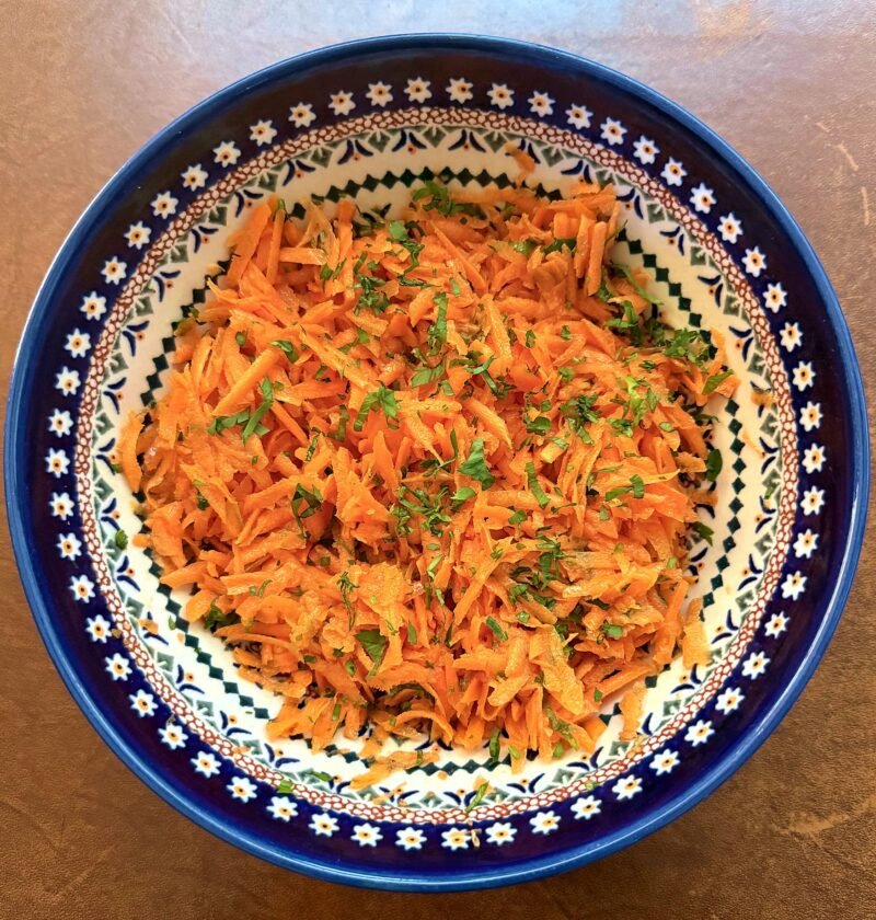 Classic grated carrot salad with fresh parsley in a blue Polish pottery bowl