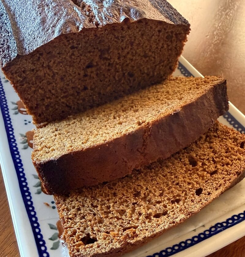 Sliced French spice bread (pain d'épices) loaf on a white platter with a blue dotted rim